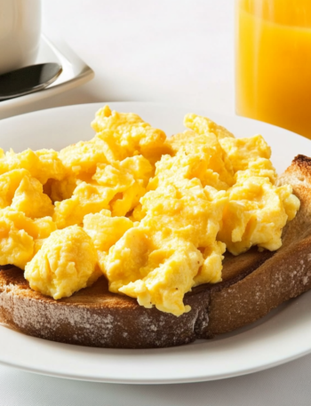 a cozy breakfast tables with scrambled eggs and a cup of juice and a coffee cup